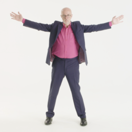 a man in a suit and pink shirt stands with legs and arms outstretched