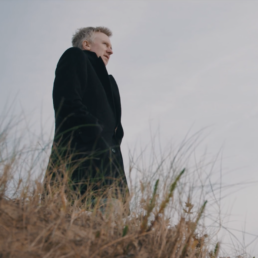 Poet Paul Farley. Dressed in black on a cold dune. Staring out to sea.