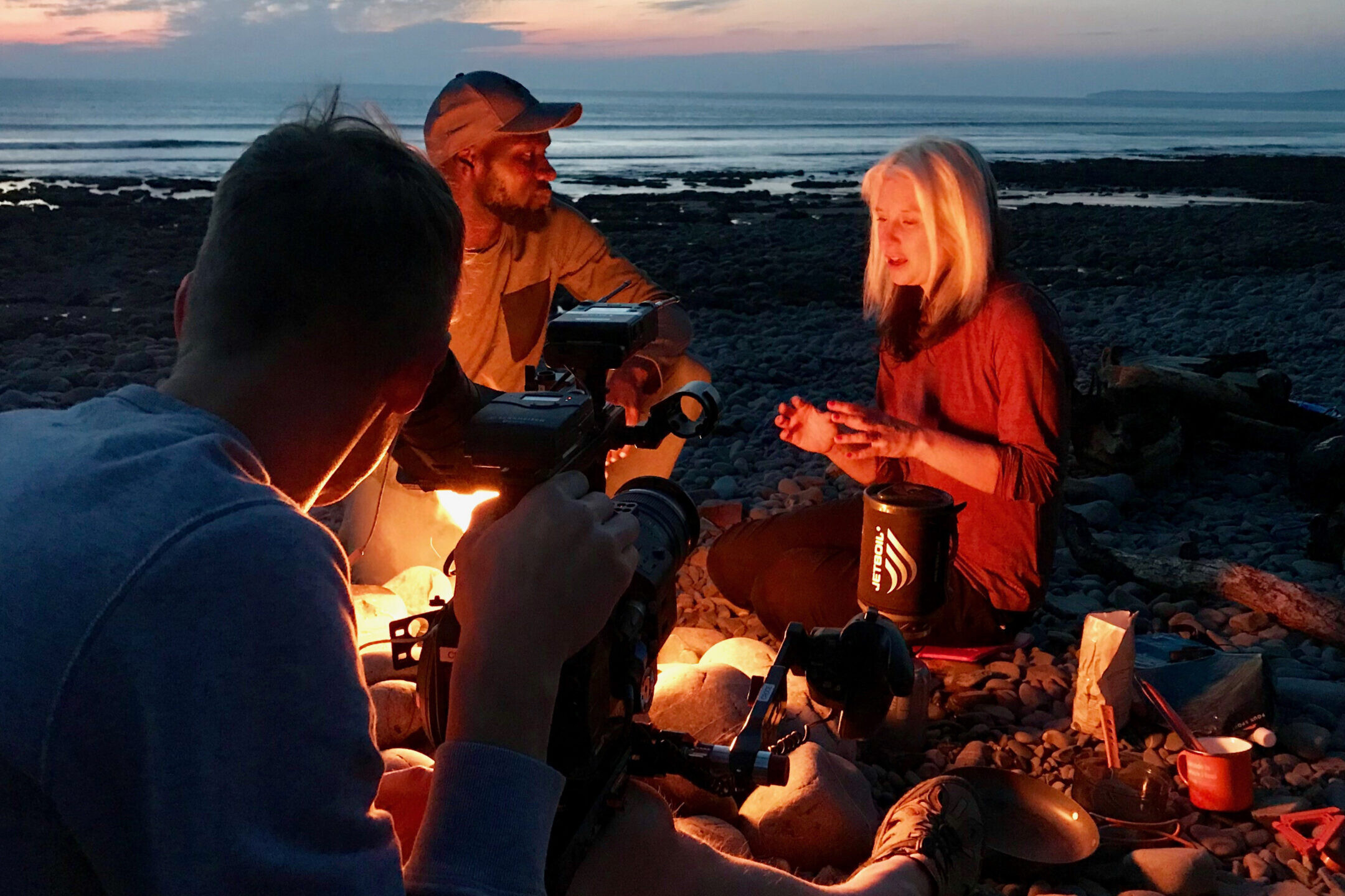 Phoebe Smith and Dwayne Fields sit by a fire on a beach