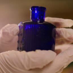 Gloved hands hold a blue poison bottle.