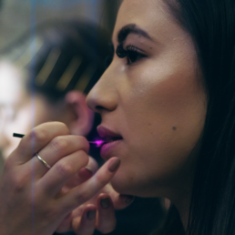 A beautiful female model has glowing pink lips gloss applied by a make up artist.