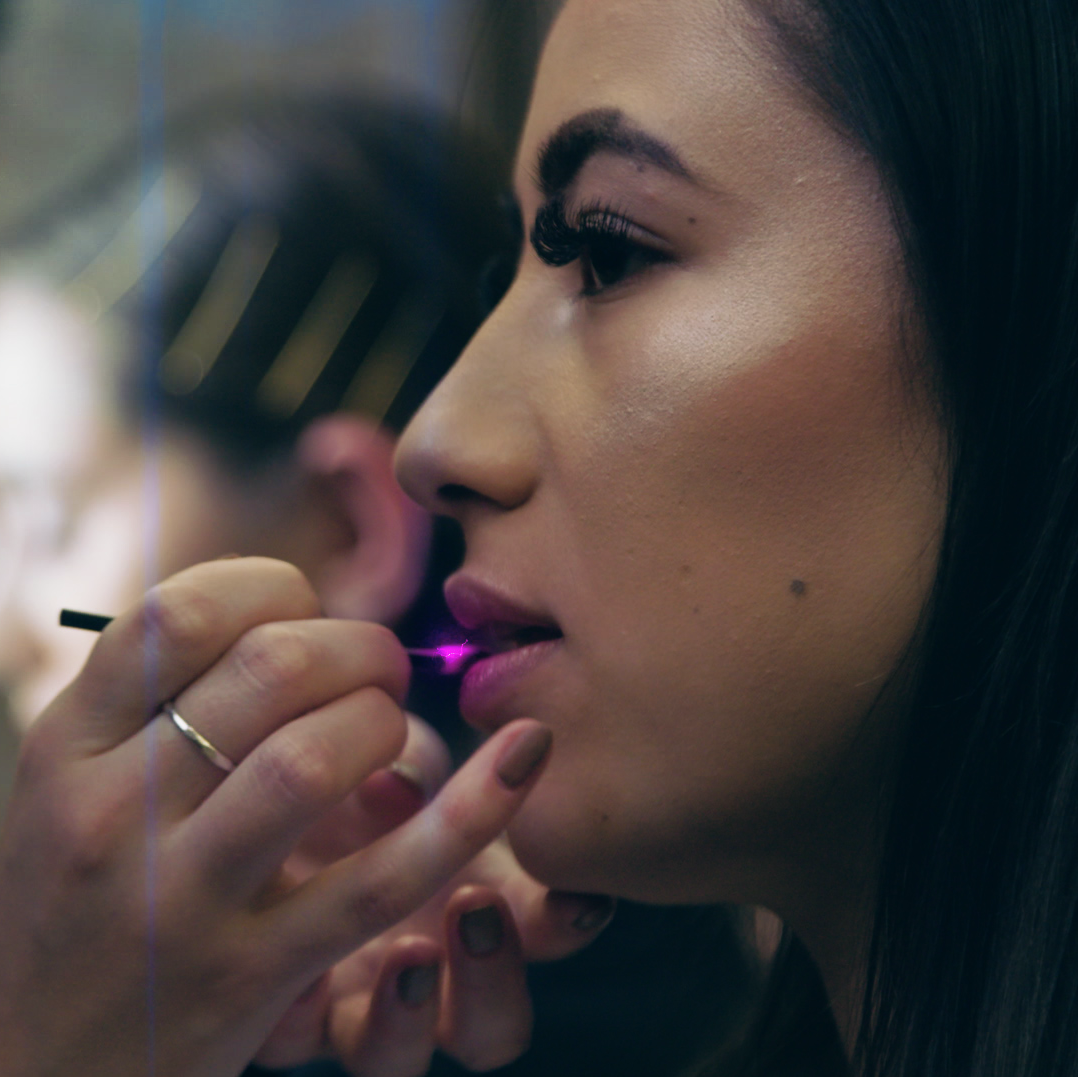A beautiful female model has glowing pink lips gloss applied by a make up artist.