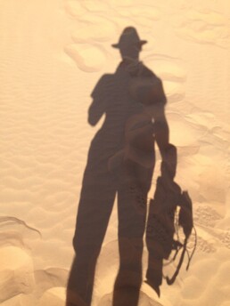 The shadow of Chris Jones holding a camera cast on desert sand